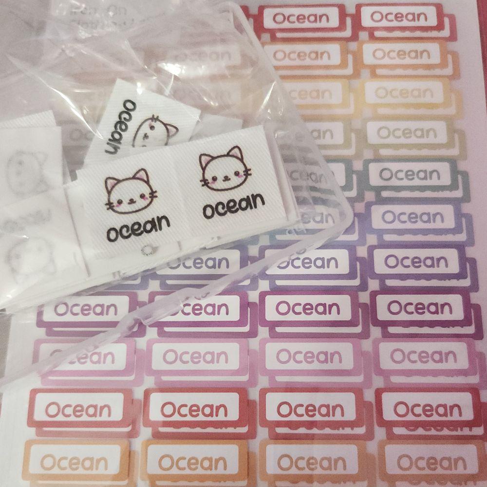 iron-on clothing labels. one set is small squares with a picture of a cartoon kitten face and the name "ocean" beneath. the second set is small rectangles with the name "ocean" in the center of a border, in a series of rainbow colours.