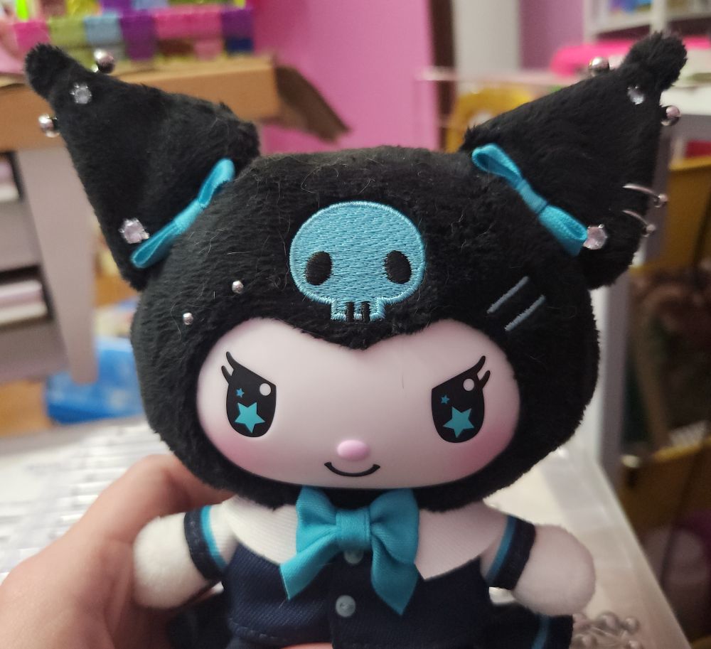 a kuromi plush with bilateral sparkly rhinestone studs in her ears, with matching horizontal barbells near the point of each ear. her left ear (viewer's right) has two horseshoe-shaped barbells near the bottom. she also has an eyebrow piercing on her right side.
