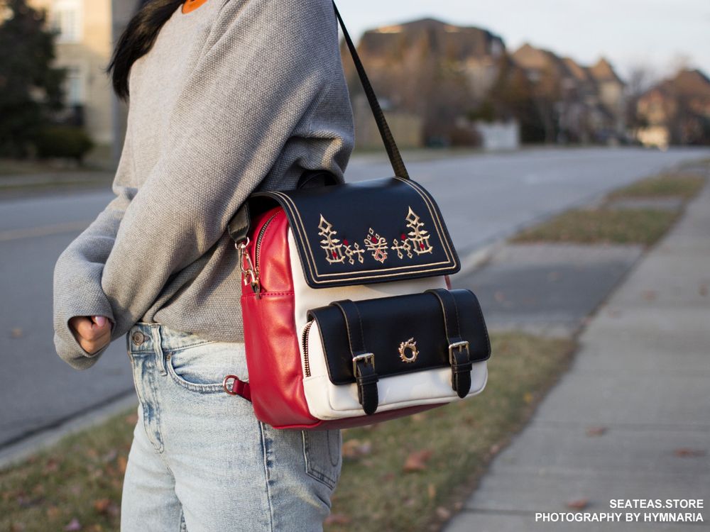 A backpack that can be transformed into a bag. It has G'raha Tia's shirt design embroidered on the front with gold hardware of the Meteor icon. This image is the model wearing it in bag mode. 