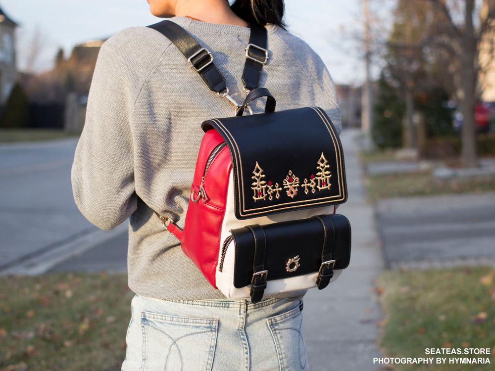 A backpack that can be transformed into a bag. It has G'raha Tia's shirt design embroidered on the front with gold hardware of the Meteor icon. This image is the model wearing it in backpack mode