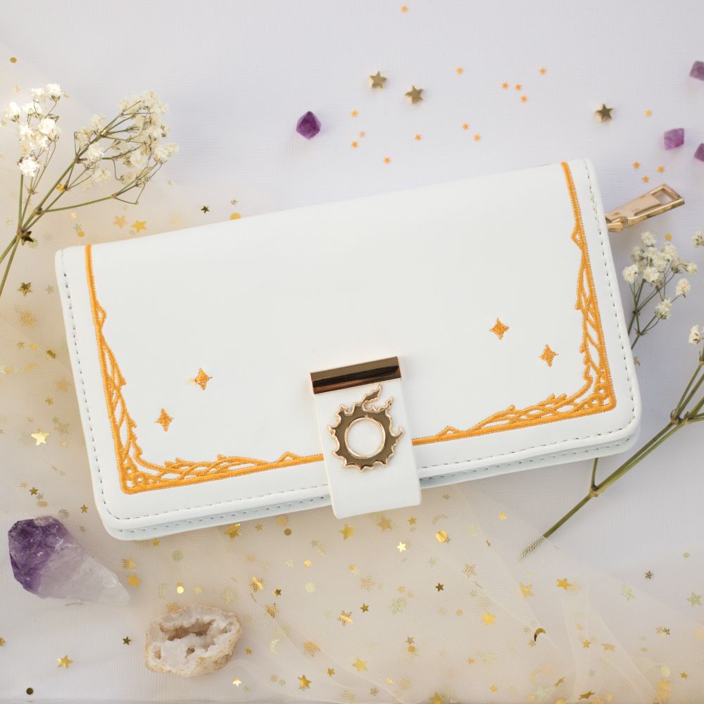 A white clutch style wallet with the meteor symbol from FF14. There is gold embroidery to mimic the menu style in the game.