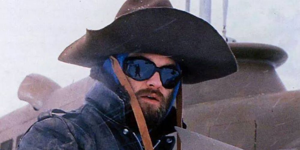 Photo of Kurt Russell as R.J. MacReady from The Thing (1982). He's bearded, wearing dark sunglasses and a giant, brown hat with a completely impractical brim that is extremely awesome.