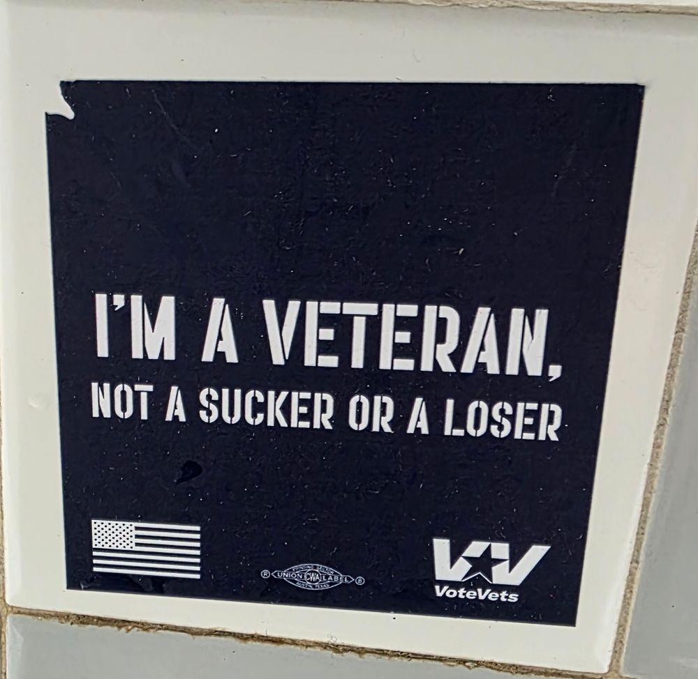 Square sticker with a dark blue background. In white letters it reads 
I'M A VETERAN, NOT A SUCKER OR A LOSER.
Lower left corner is an American flag. Lower right corner is the logo for Vote Vets with Vote Vets spelled out under the logo. 