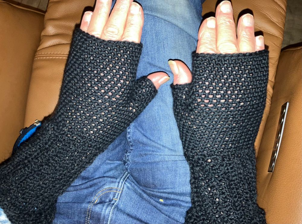 Twee handen met zwarte polswarmers.  Boven een spijkerbroek. 