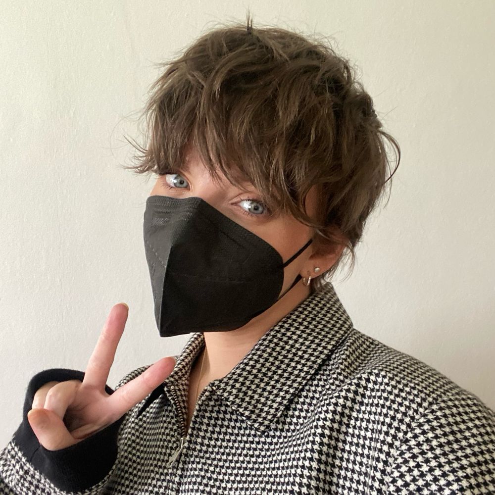 Jenny, a white slim woman with short dark hair, wears a black respirator mask.
