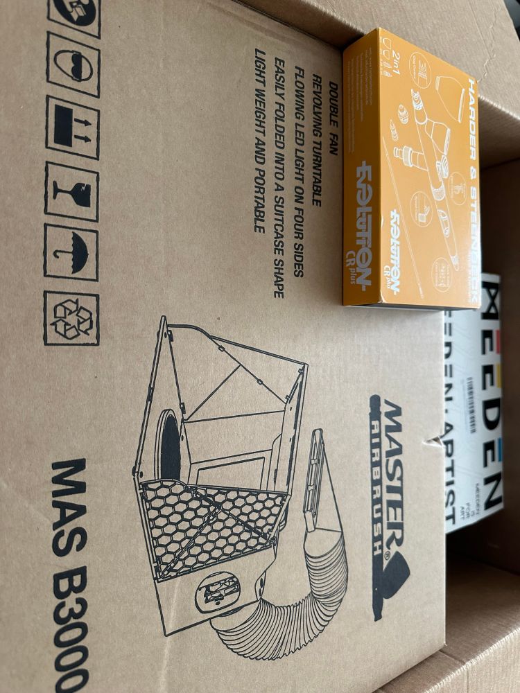 Boxes containing the equipment need for an airbrush setup. There is an airbrush on top of paint box with a compressor behind them.