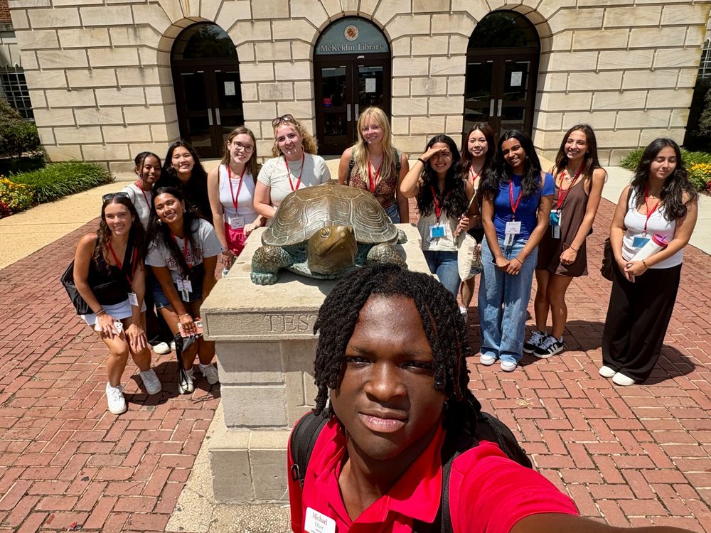 Orientation advisor taking a selfie with a group of incoming freshmen in front of McKeldin Library