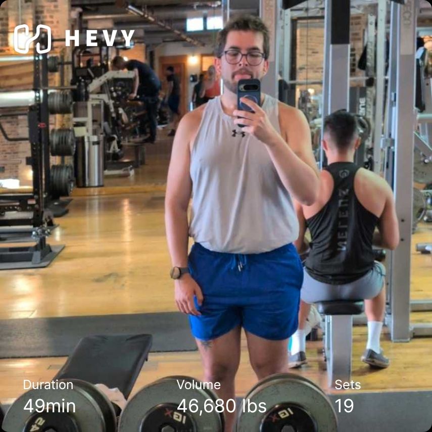 Gym mirror selfie of me in a grey tank and blue shorts. I'm sticking my tongue out. Hevy workout info included 