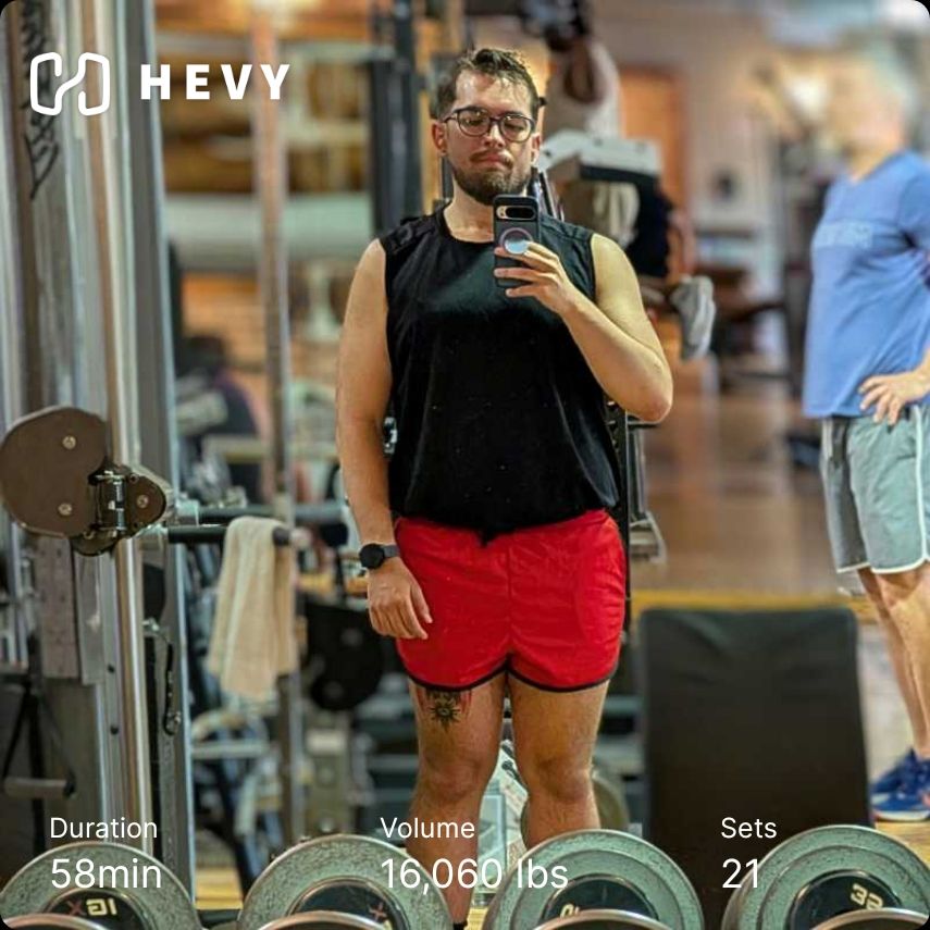 Gym mirror selfie of me in a black tank and red shorts. Hevy workout info included 