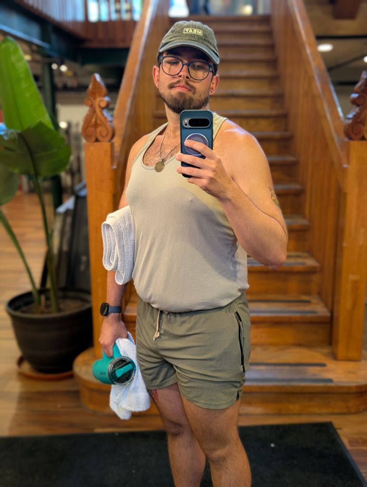 Gym mirror selfie of me in a grey tank, green MEAT shorts, and grey MEAT hat. 