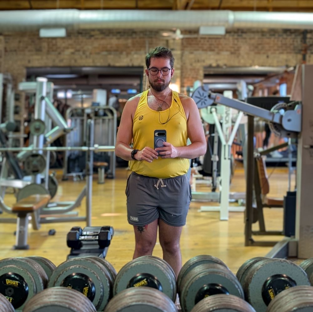 Gym mirror selfie of me in a yellow tank and grey shorts.