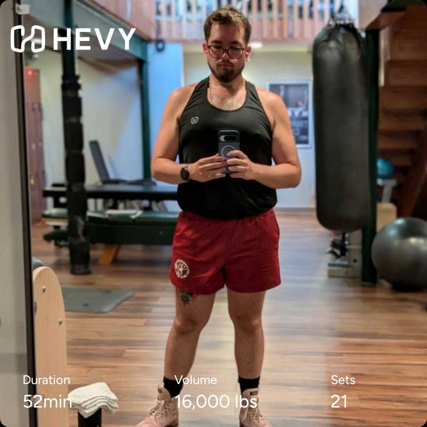 Gym mirror selfie of me in a black tank and red shorts. Hevy workout info included 