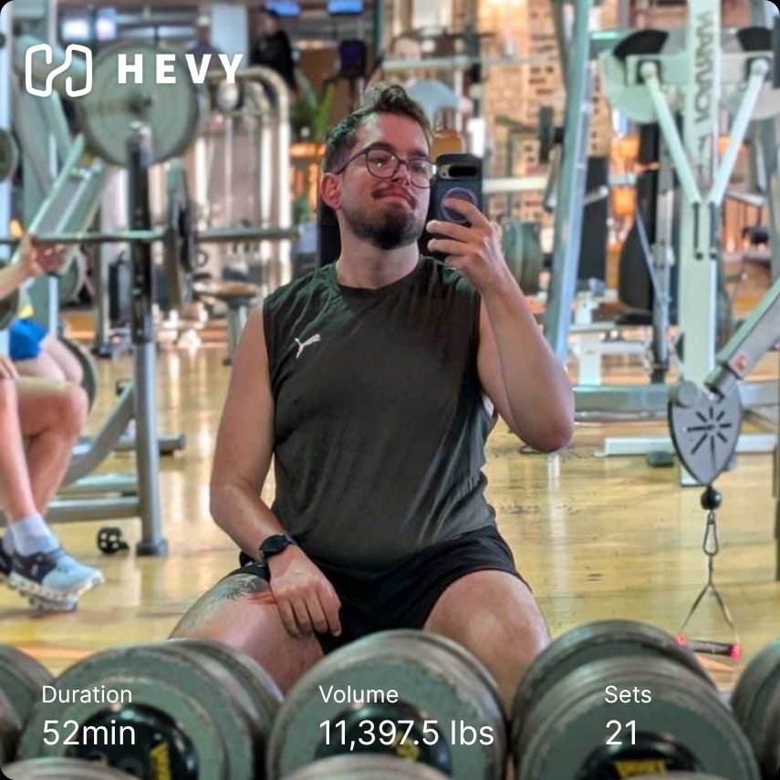Gym mirror selfie of me in a green tank and black shorts sitting on a bench. Hevy workout info included 