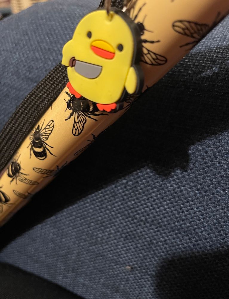 A yellow duck with a knife keyring attached to a yellow walking stick with black bees on it 