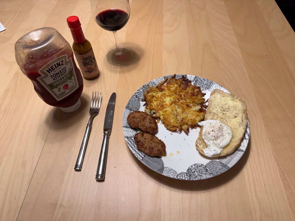 A breakfast. Left to right: ketchup, hot sauce, sausage patties, hash browns, and toast with a poached egg on it.

And a glass of wine for some reason.
