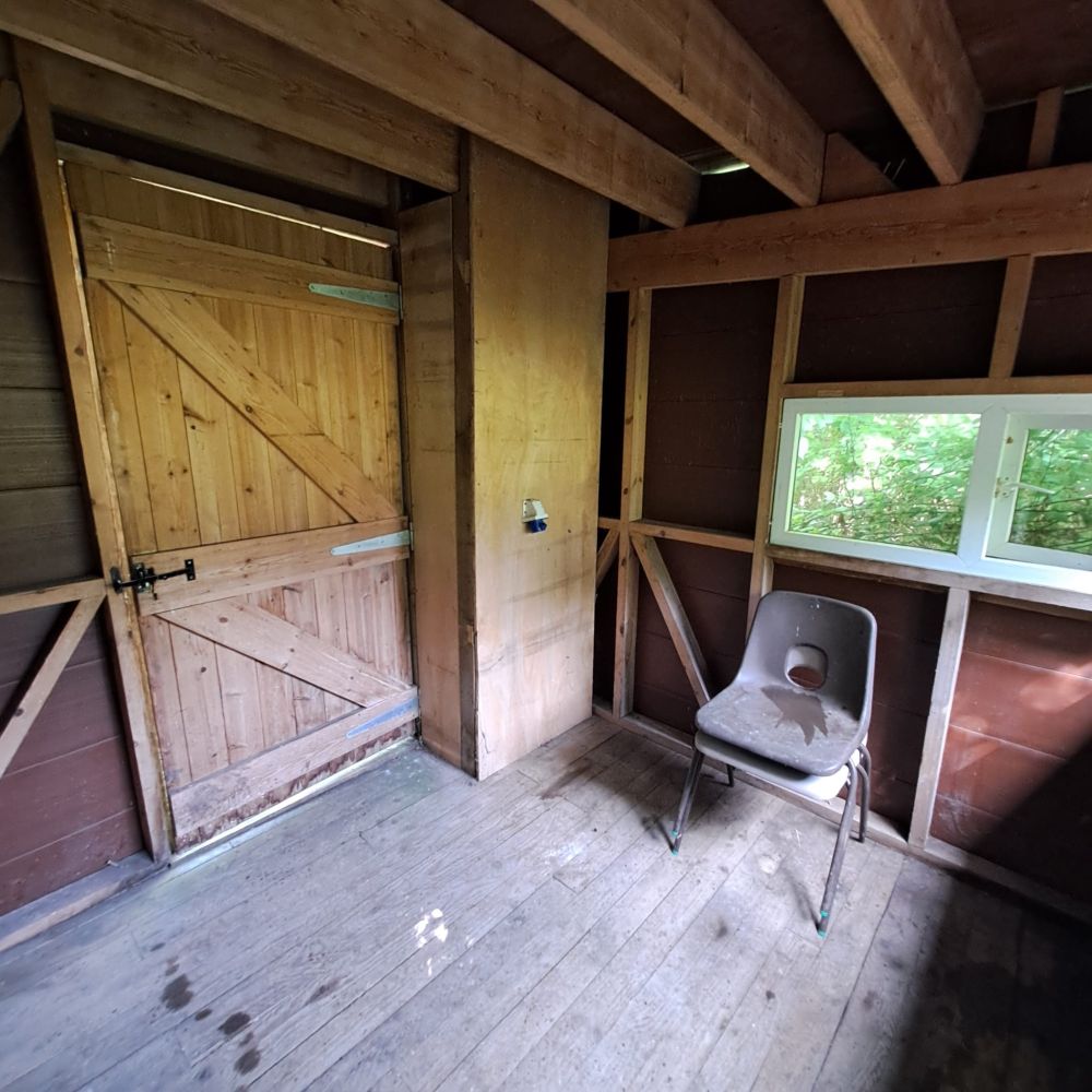The interior of a wooden bird-hide, with the door on the left and window and chairs on the right. Everything is spotless!