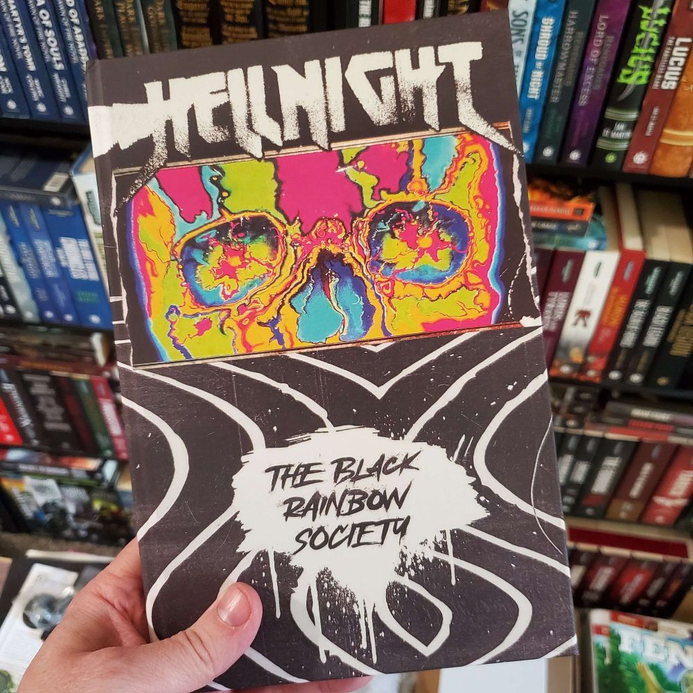 The cover of The Black Rainbow Society from Gavriel Quiroga. Says Hell Night at the Top, The Black Rainbow Society at the bottom, and has a trippy image of the eyes and nose of a skull in the middle in yellows, blues, pinks, and greens. 