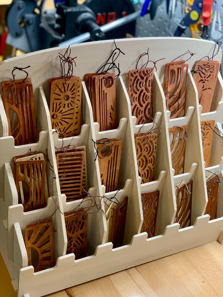 Wooden bookmarks with various cutout designs, aitting in a wooden bookmark display holder thingy