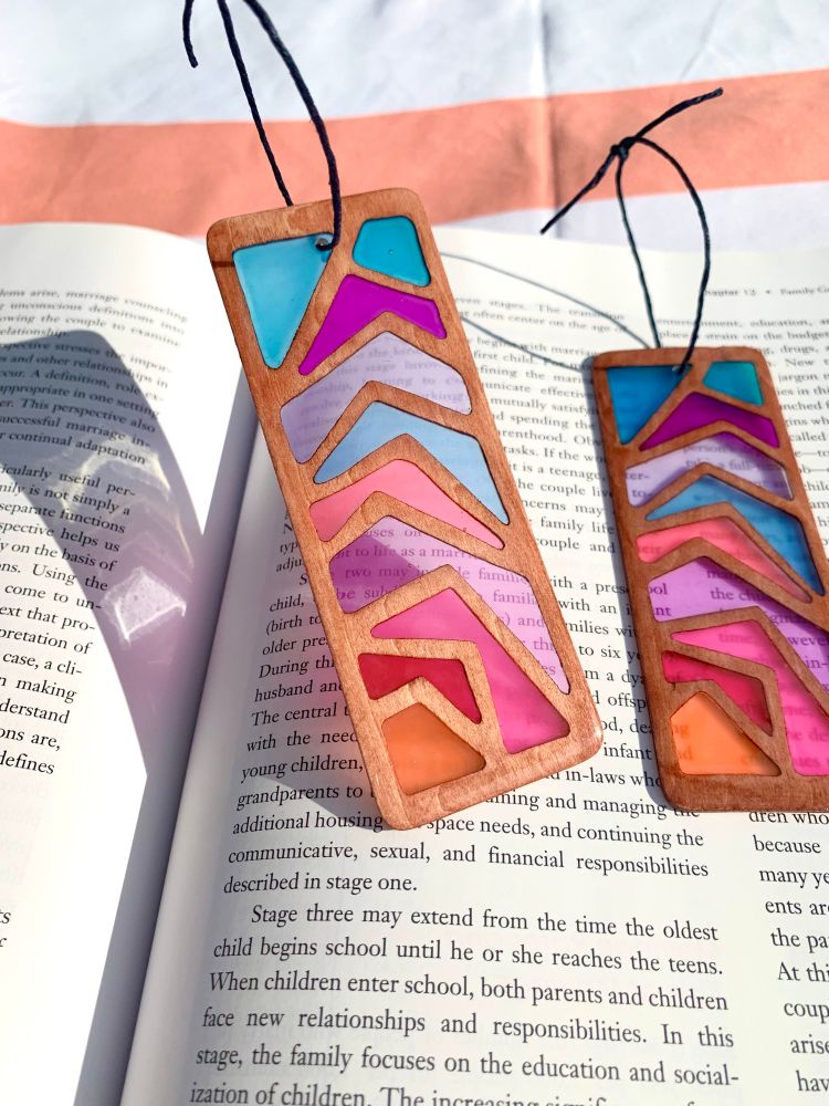 Zaigzag wood & resin bookmark displayed on an open book, sun shining through the colorful design.