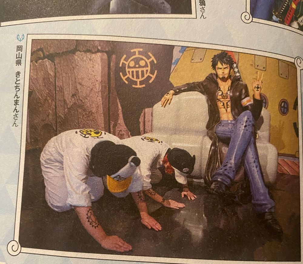 It’s Penguin and Shaichi cosplayers (from one piece) bowing on the ground at an open coat shirtless Trafalgar Law statue. Caption to the left says, in Japanese ‘Okayama Prefecture, Kitochiman-San’ (naming the cosplayer that submitted the image) 