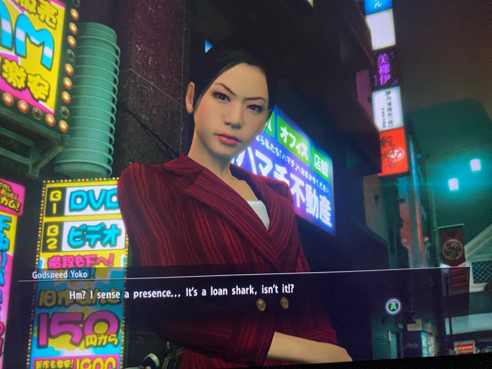 It’s a screenshot from Yakuza Kiwami. A woman in a red work suit with a white shirt, with black hair in a bun, looks down at the camera with suspicion. Behind her, it’s night, and the city lights glow.

Dialogue
Godspeed Yoko: Hm? I sense a presence… It’s a loan shark, isn’t it!?