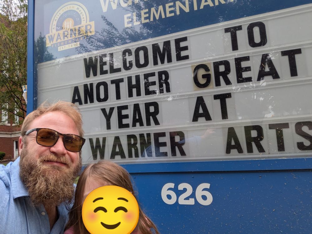 A selfie with Daniel and his daughter in front of a school sign saying "Welcome to another great year at Warner Arts"
