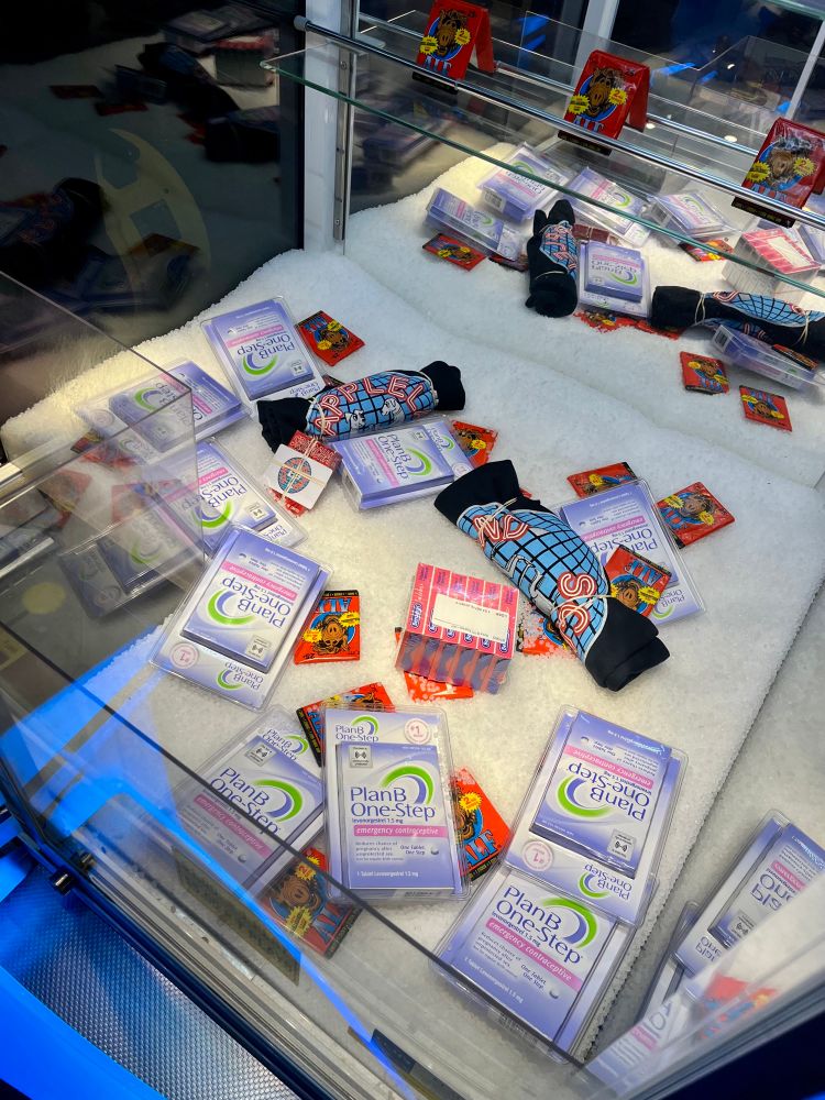 Prizes inside the claw machine include: T-shirts, gift cards, playing cards, Alf cards, Benadryl, and  Plan B One-Step.