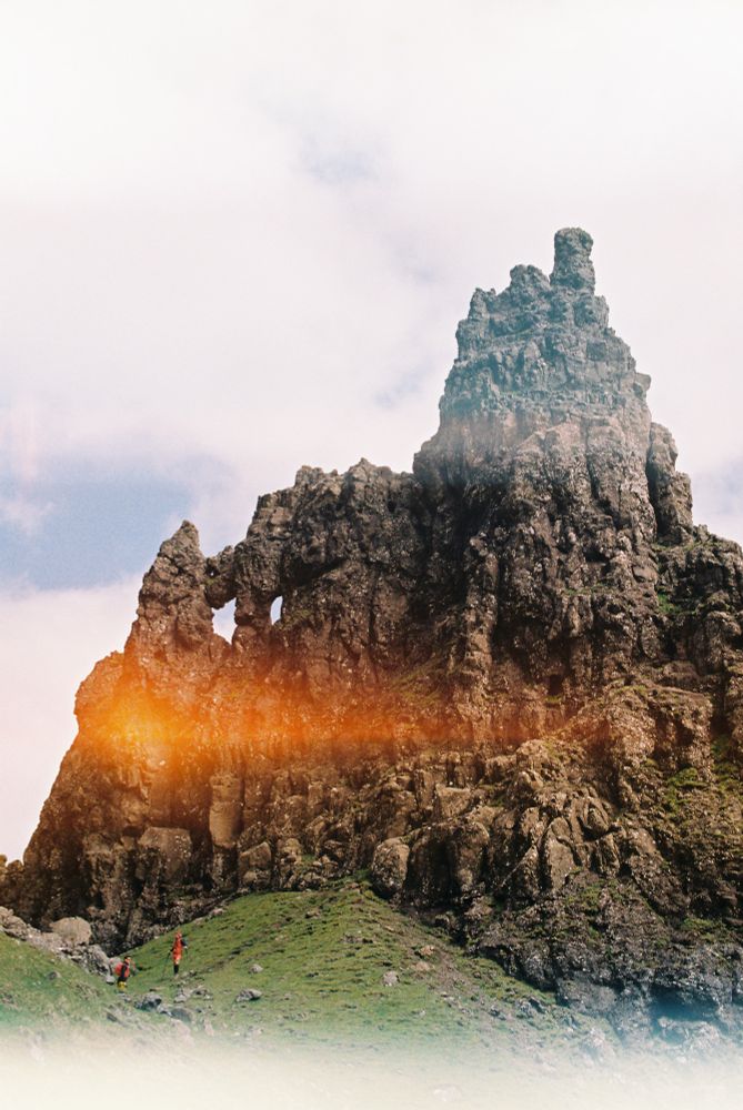 Film photo of the old man of storr. Small brightly colored hikers are dwarfed by a monolithic rock. By moth snow.
