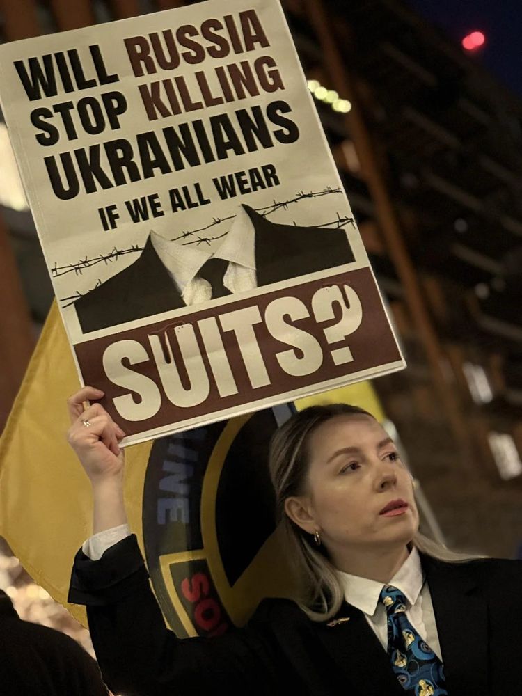 London protestor with a sign aimed at the Current Unstable Nutjob Tyrant (Trump) that states "Will Russia Stop KIlling Ukrainians If We All Wear Suits?"