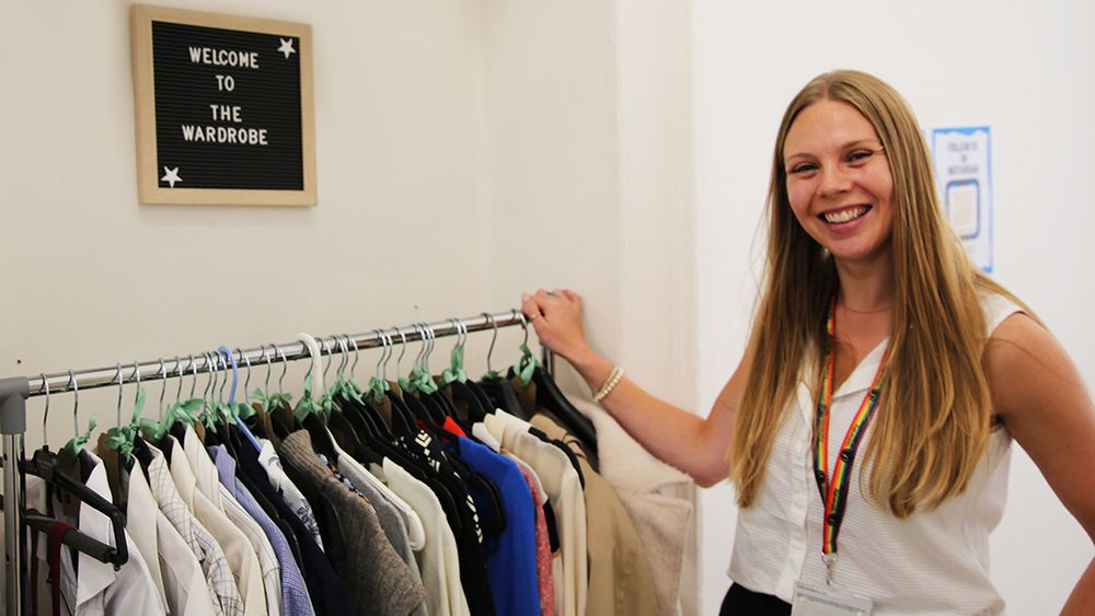 Student standing beside a rail of donated interview clothing