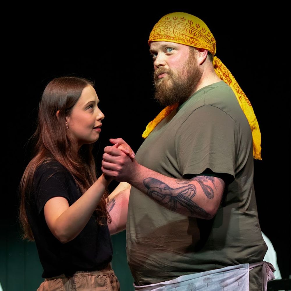 Two actors sat on a stage, looking upset, side by side. 
