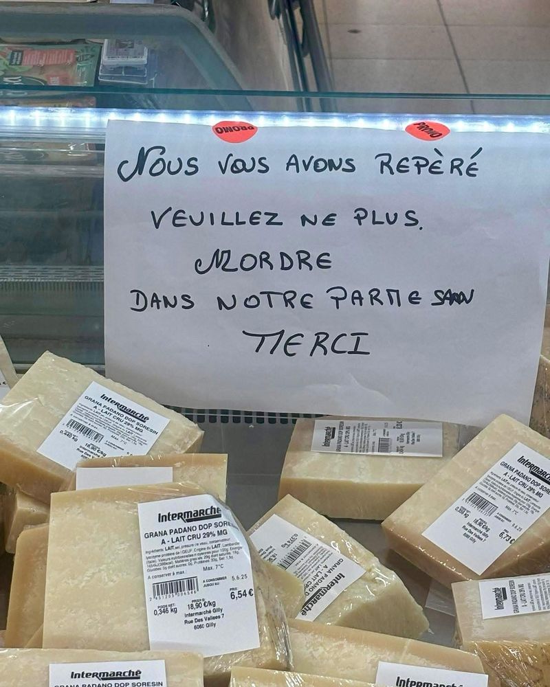 Petite affichette de supermarché qui dit « Nous vous avons repéré - Veuillez ne plus mordre dans notre parmesan - Merci »