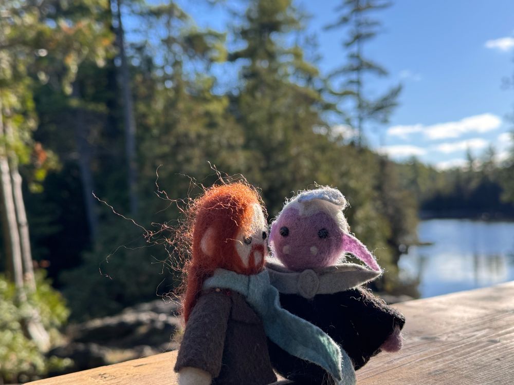 tiny felted toys of Essek Thelyss and Caleb Widogast in front of a sunny scene of trees and water