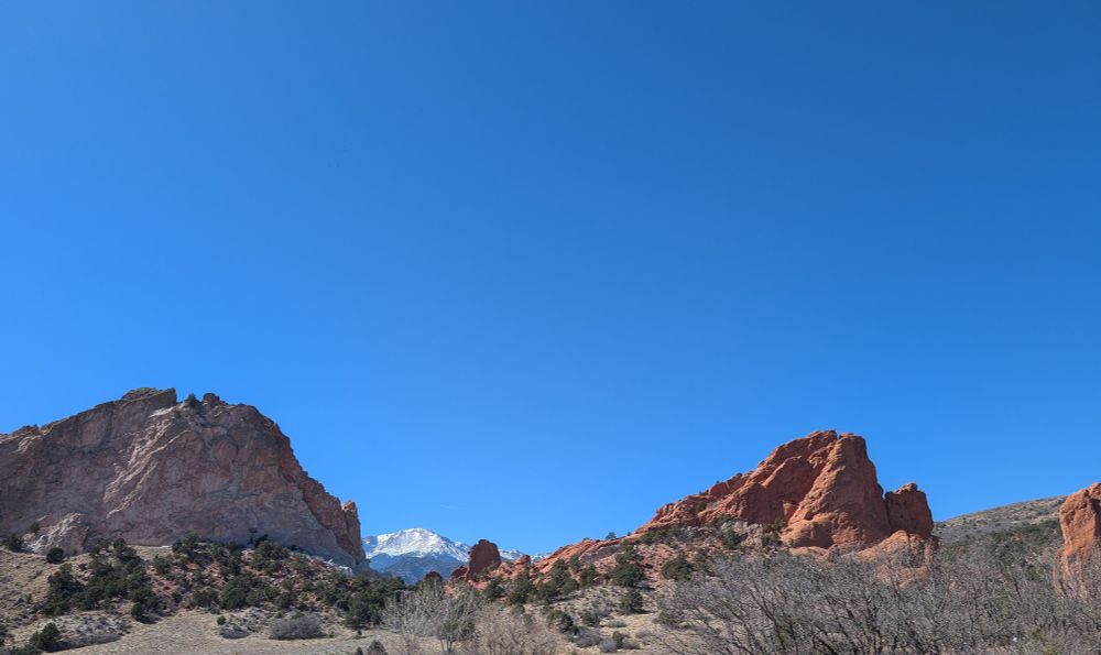rocky red mountainous terrain with snow-dusted pike's peak in the background and insanely blue sky
