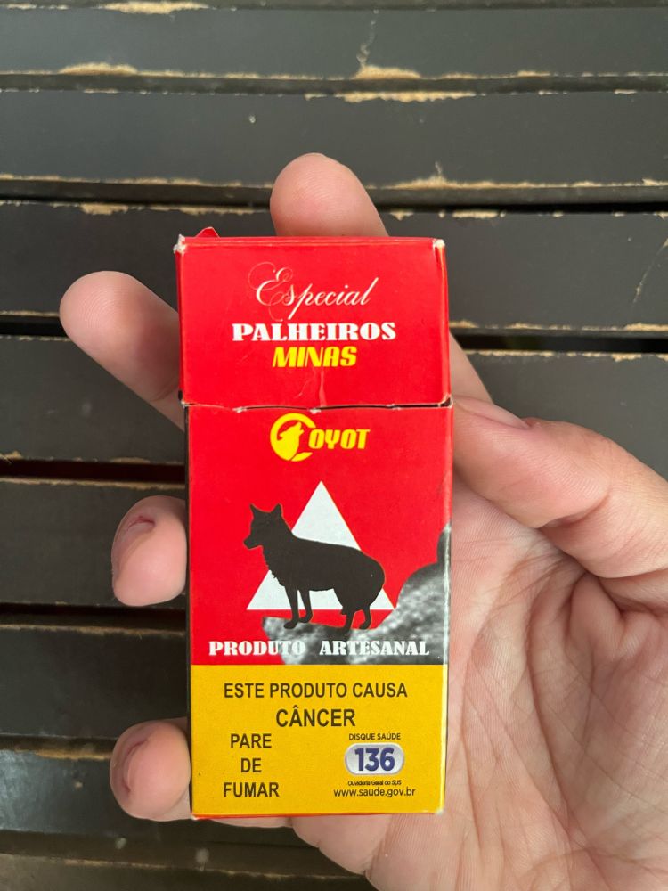 Mão segurando uma caixa do cigarro de palha da marca COYOT, imitação da marca COYOTE. Todo o design é parecido, mas o cigarro é muito ruim.  