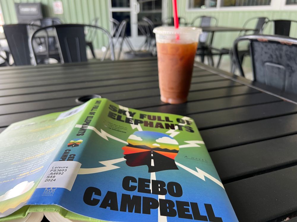 The book Sky Full of Elephants on an outdoor table with an iced coffee