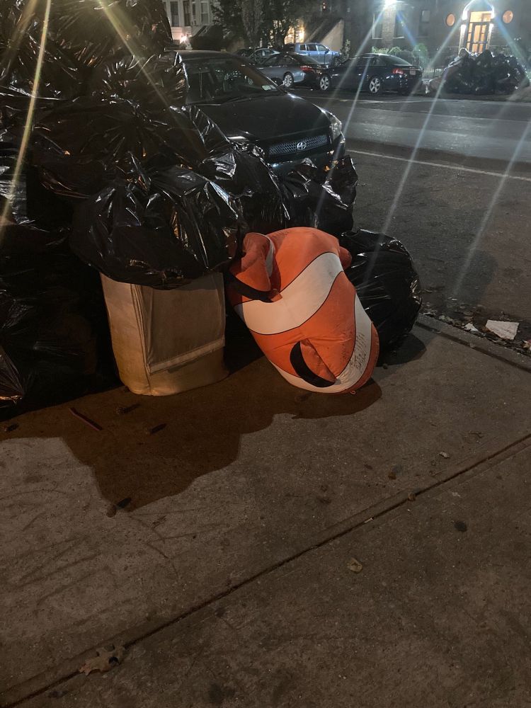 A Nemo plushie in a heap of garbage bags on a sidewalk