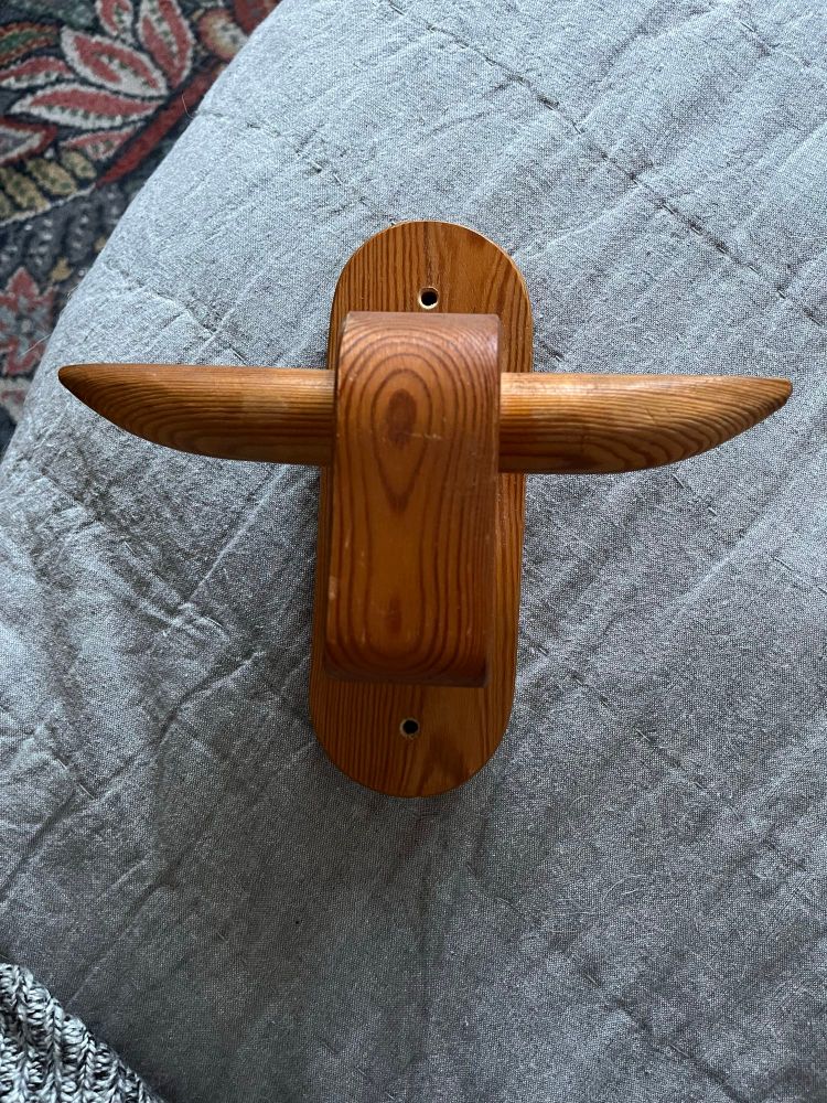 En träskulptur i furu i formen av ett stiliserat oxhuvud med utstickande horn som man kan använda som krokar. Sitter på en platta i samma trä som kan fästas i väggen.
Signatur på baksidan: Form: Håkan Undén, Sigtuna
