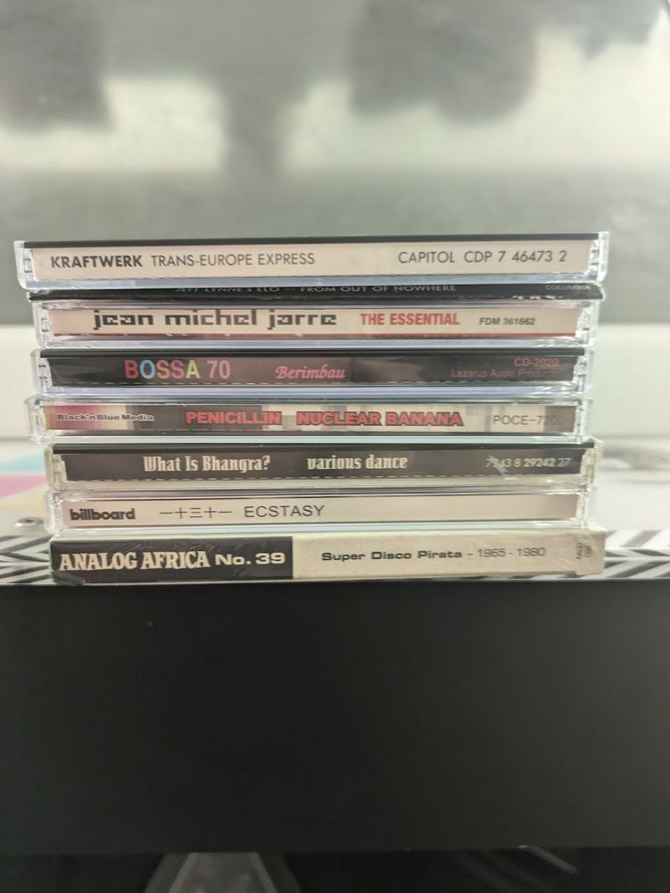A stack of CDs on top of a BeatStream cabiner.
In order:
Kraftwerk - Trans-Europe Express
Jeff Lynne's ELO - From Out of Nowhere
Jean-Michel Jarre - The Essential
Bossa 70 - Berimbau
Penicillin - Nuclear Banana
What is Bhangra?
一十三十一 - Ecstasy
Super Disco Pirata