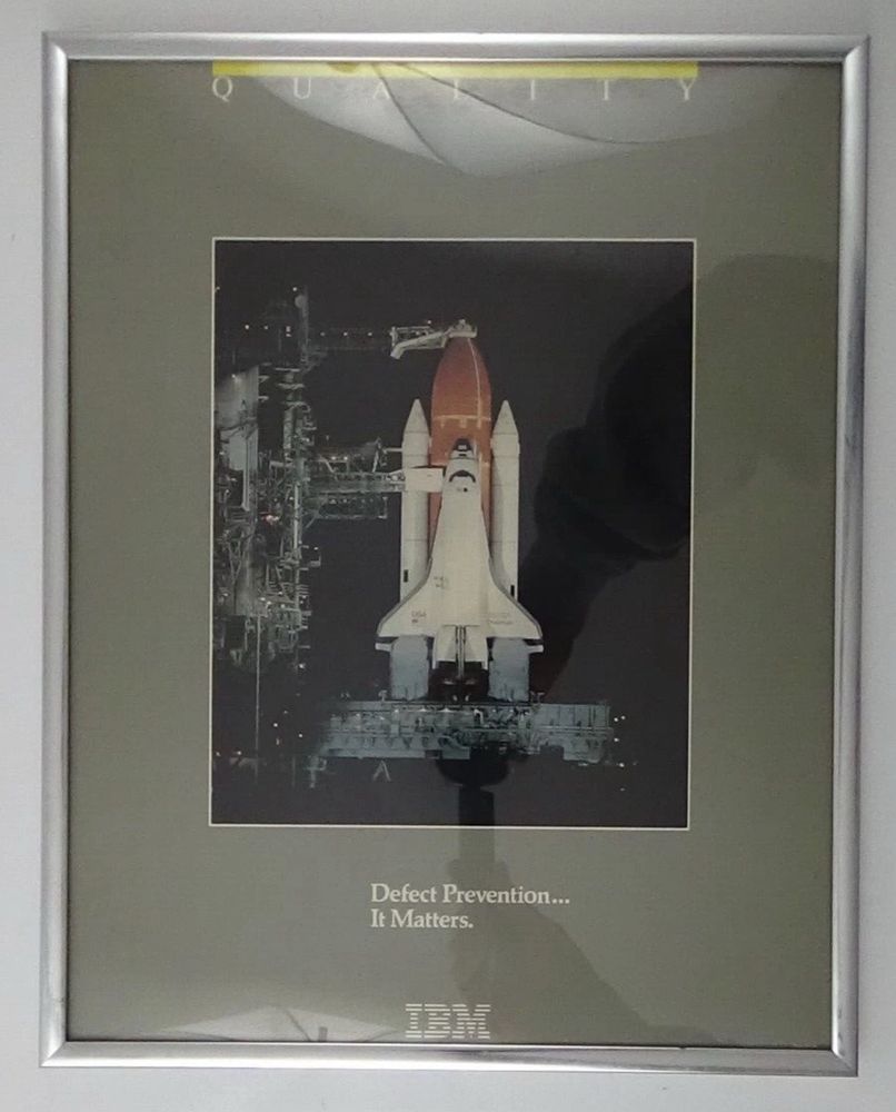 A framed 14x11 motivational poster from IBM. It has a gray background. The header says “Quality” and there is an inset frame of Challenger on the launchpad. The bottom says “Defect Prevention… It Matters.” with a classic IBM logo in white.