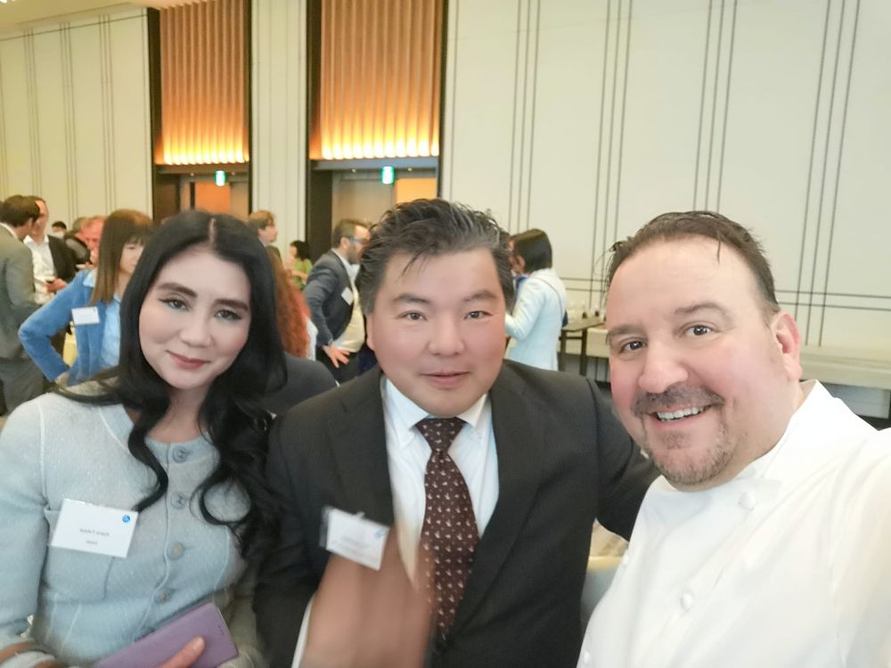 スーツ姿の榊原平とシャネルを着こんだ女性、シェフと三人が立っています。