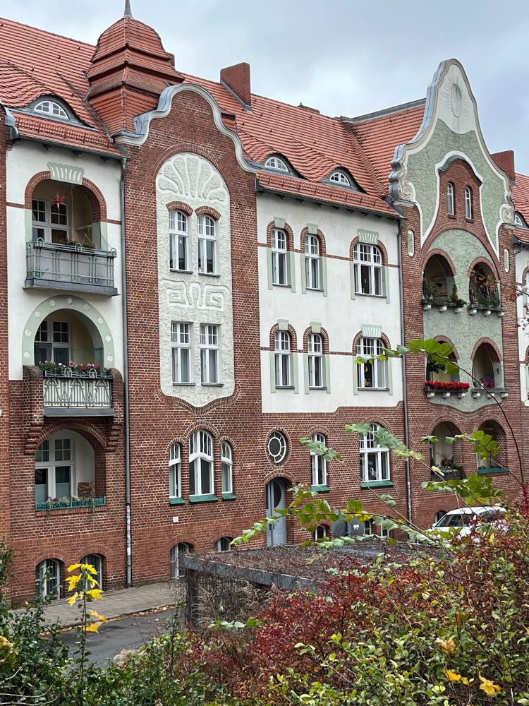Altes Bürgerhaus aus Ziegeln mit zurückgesetzten Balkons, großen Fenstern und Putz in verschiedenen Farben und Formen 