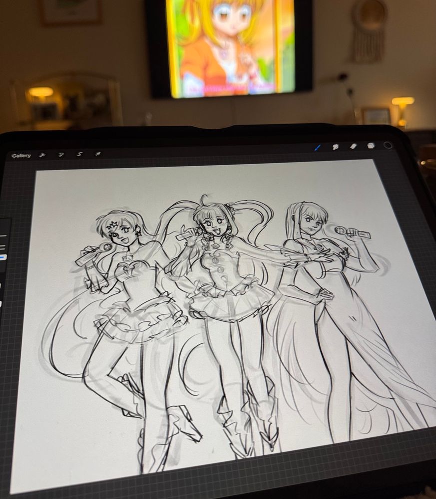 a photo of a living room with an ipad held up the camera. the tv in the background is playing an episode of mermaid melody pitchi pitchi pitch, and the ipad is displaying a wip drawing of the three main mermaids from the series. hanon, luchia, and rina, are sketched from left to right and dressed in their first season transformation outfits, holding up their respective microphones to their mouths.