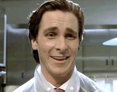 Headshot of Christian Bale as Patrick Bateman in American Psycho. -- a really handsome white dude -- brunette, pale skin, white teeth, wearing a sardonic look of surprised delight. Background, a blurry kitchen, with stainless steel cabinets. Over a white buttondown shirt and tie, he's also wearing a waterproof semi-transparent nylon raincoat like your Grandma might have had folded up in an envelope made from the same material, in her purse.