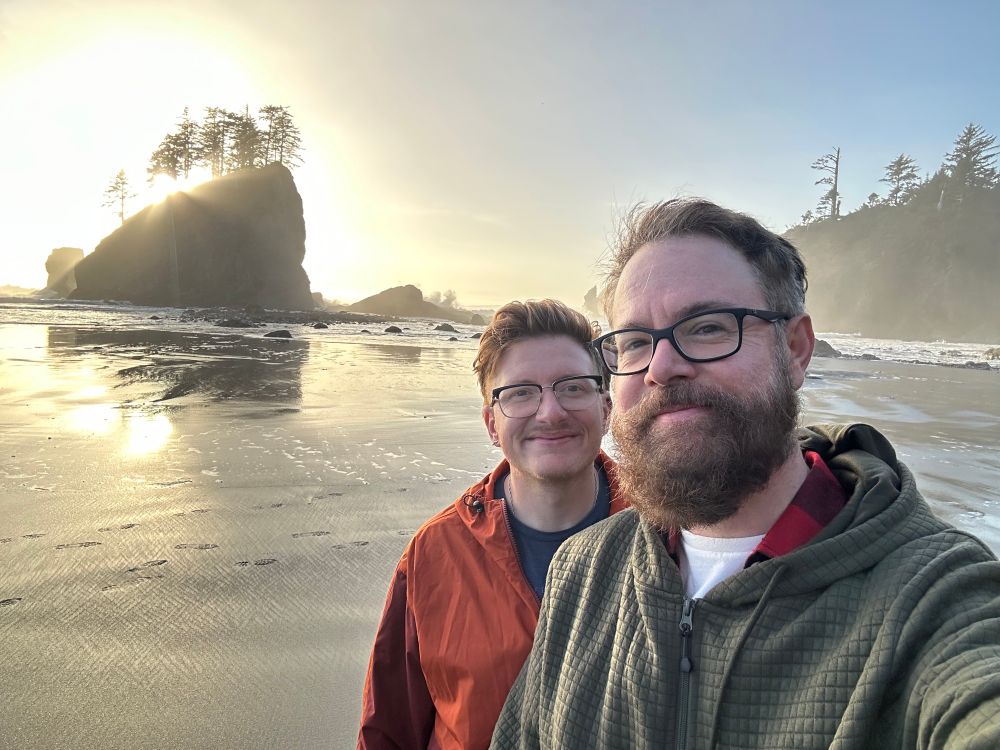 Two men in front of sea stacks as the tides goes out at sunset. 