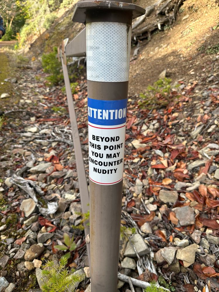 A sign on a pole reads “Attention: Beyond this point you may encounter nudity”