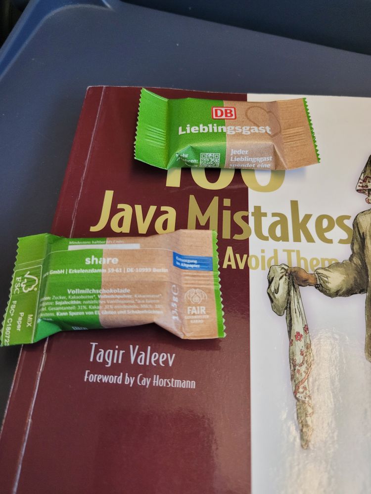 Schokolade der DB auf dem Buch '100 Java Mistakes and How to Avoid Them' von Tagir Valeev auf dem ICE Tisch.