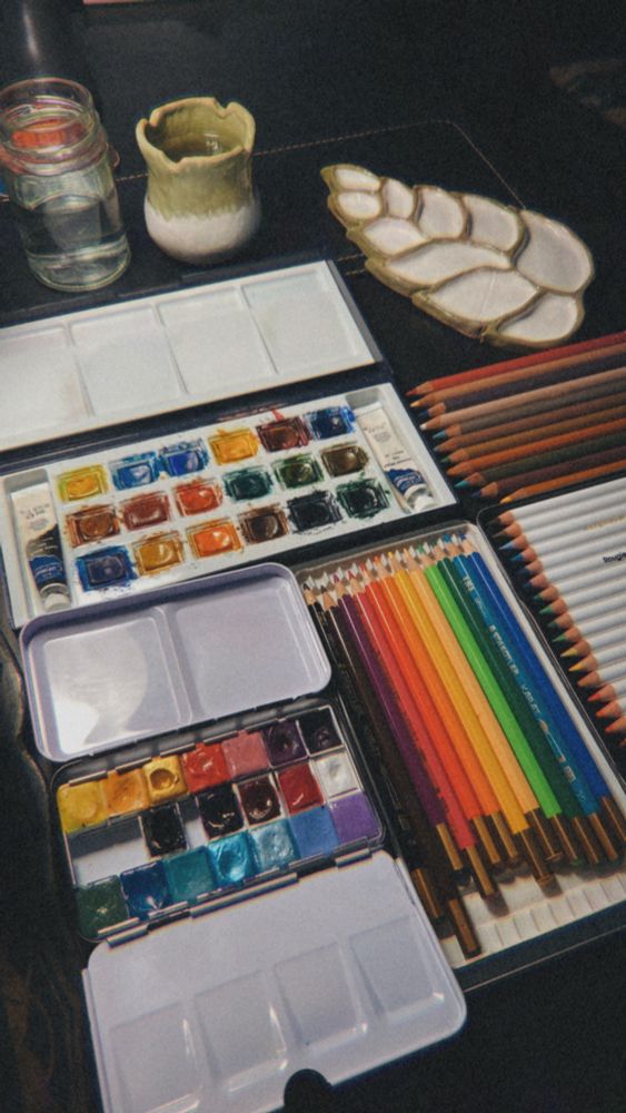une photo de mon matériel d'aquarelle, de la penture, des crayons, des pots pour l'eau et une palette en céramique en forme de feuille