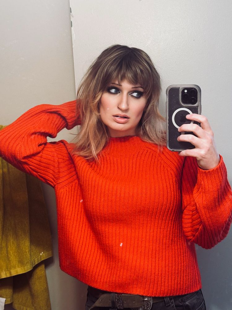 mirror selfie of phoebe in a red sweater with dark eye make up