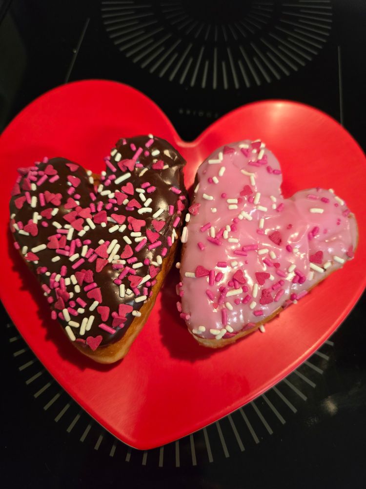 Two heart shaped doughnuts on a heart shaped plate. One is chocolateand the other is strawberry